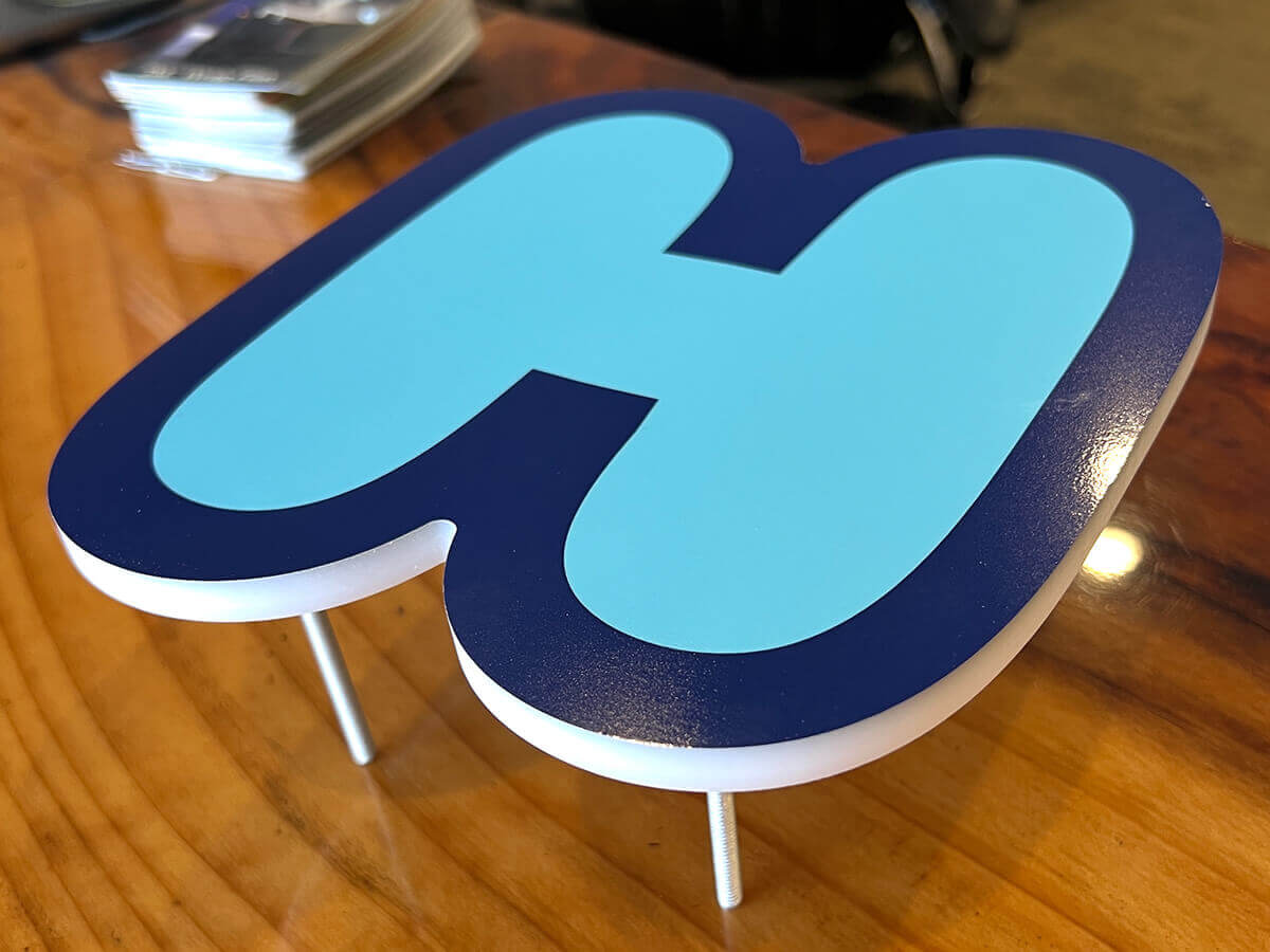 A single 3/8 inch white acrylic H letter, it also has a full color printed decal applied to the face creating dimension and aluminum threaded standoffs